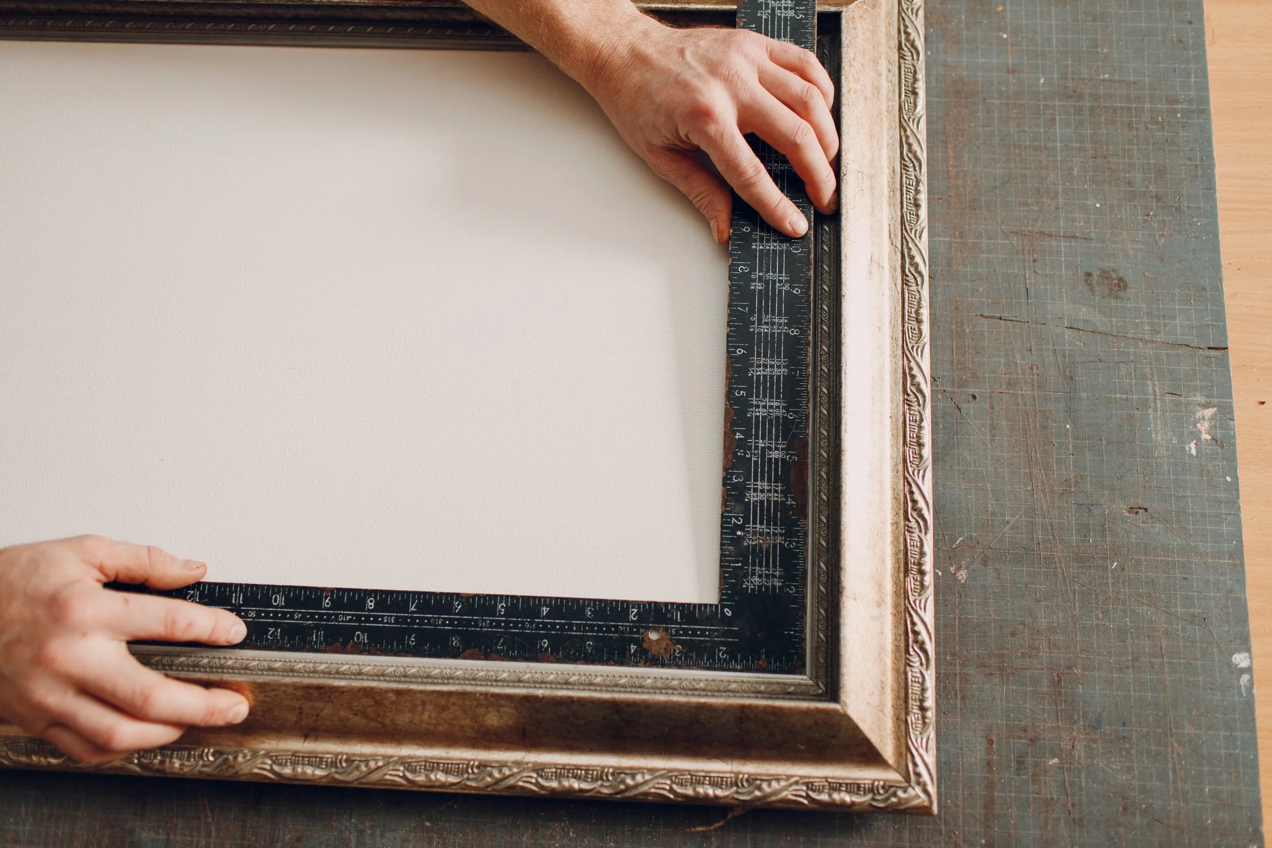 An Allart craftsman measuring a silver ornate frame by hand with a ruler in the studio