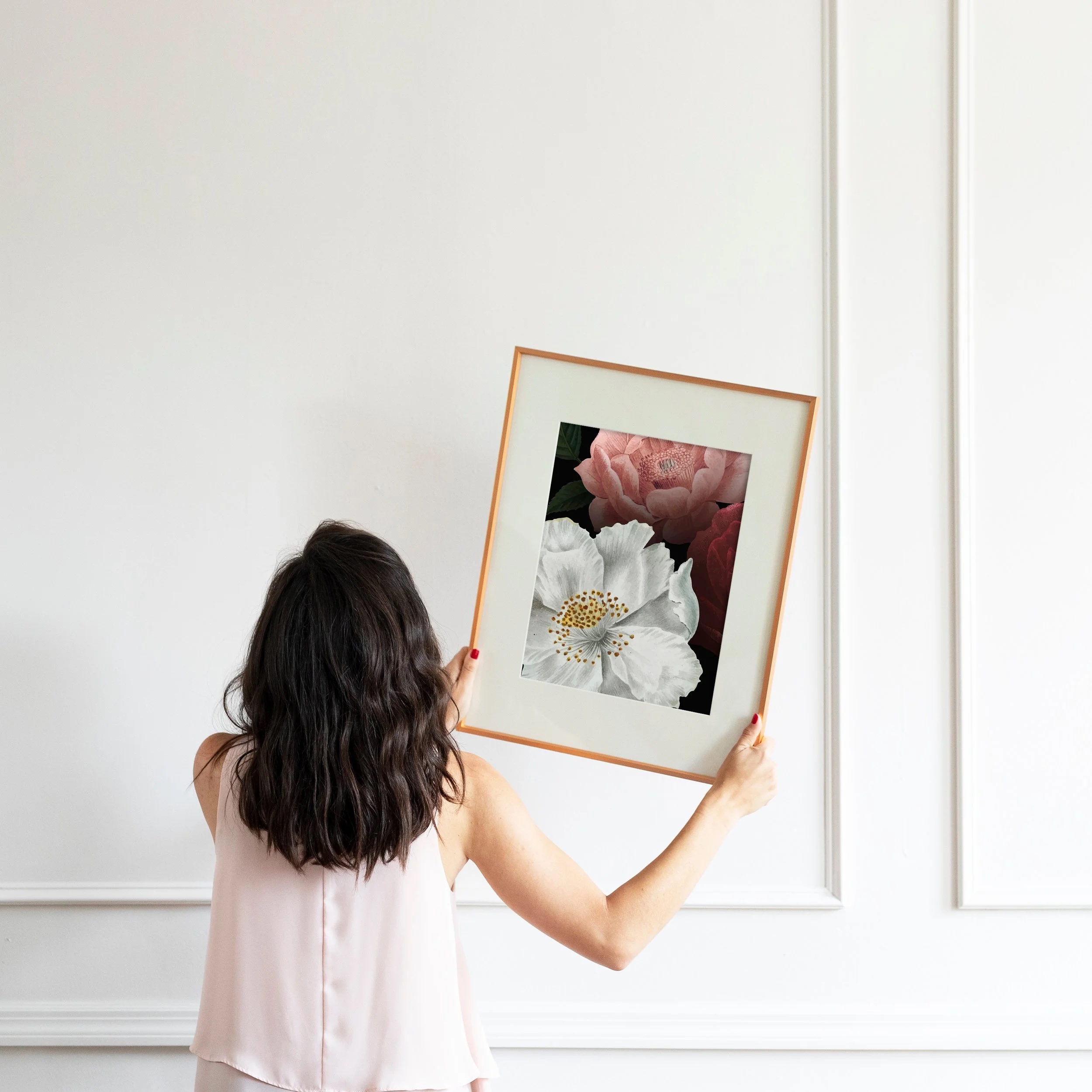 A woman hanging a custom-framed floral print in a client's home